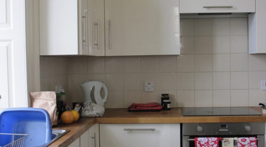 A kitchen counter with a kettle near the stovetop, a small dark jar and a blue dish rack.