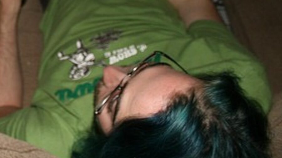 A man with glasses and dark hair lying down, wearing a green T-shirt with printed text.